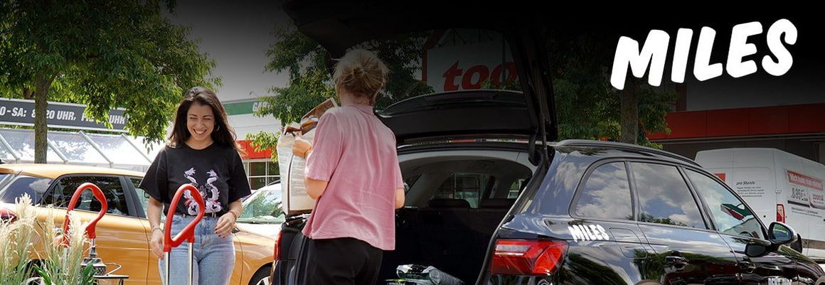 Zwei Personen laden Einkäufe in einen schwarzen Kombi